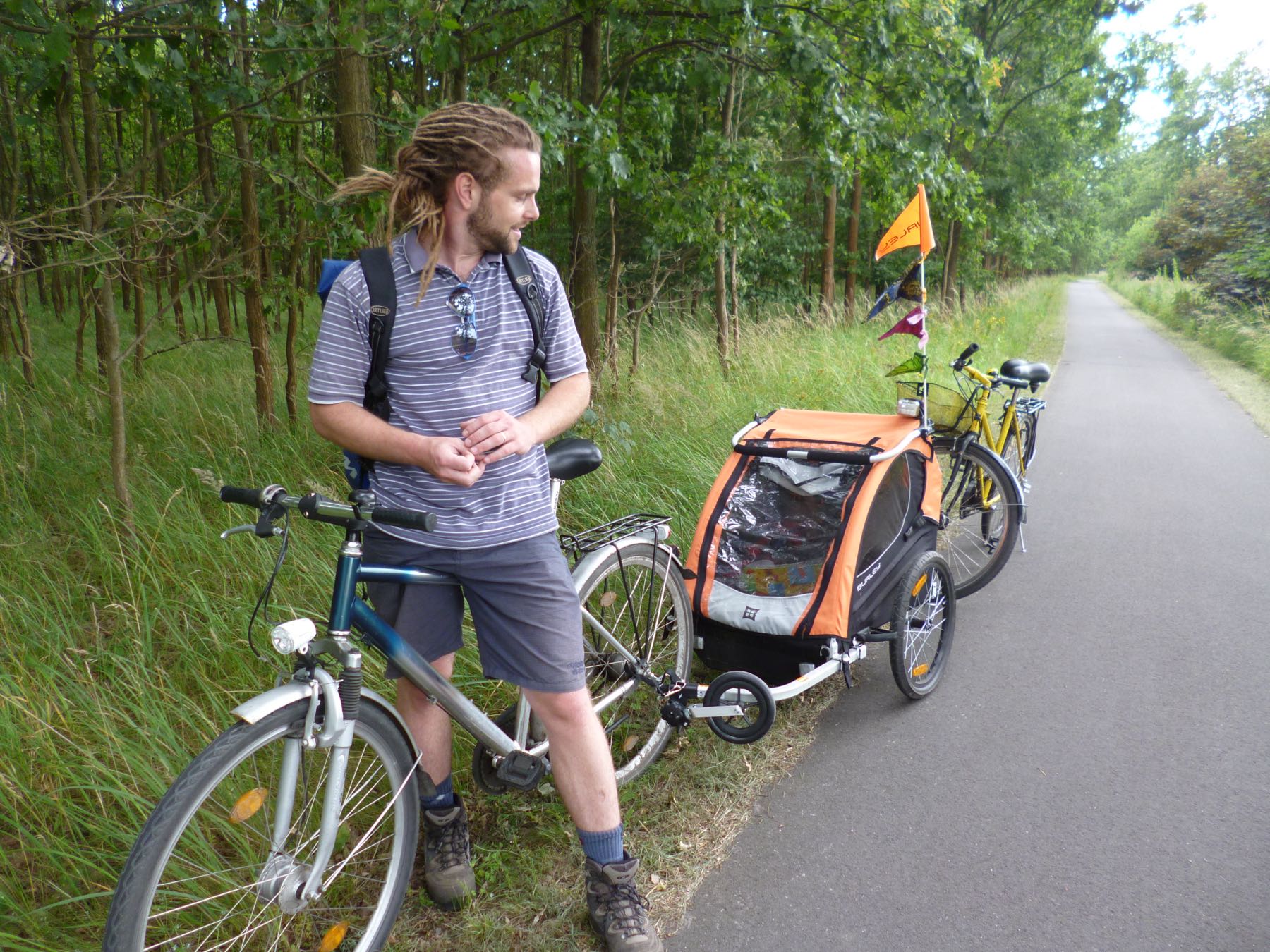 Adam con un acoplado de bicicleta para niños, en un camino arbolado de Berlín.