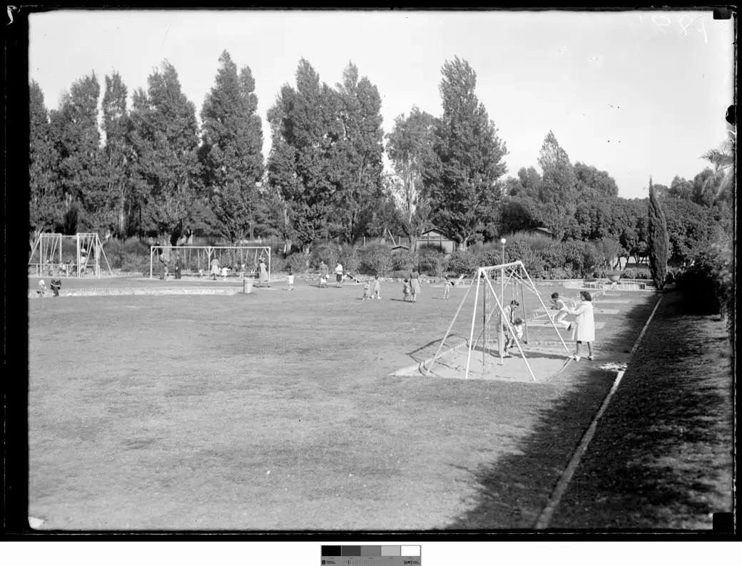 Foto histórica, 1942: un césped amplio con tres juegos de hamacas, el más cercano sobre un rectángulo de arena, chicos pequeños y algunos adultos junto a los juegos, y árboles altos al fondo.