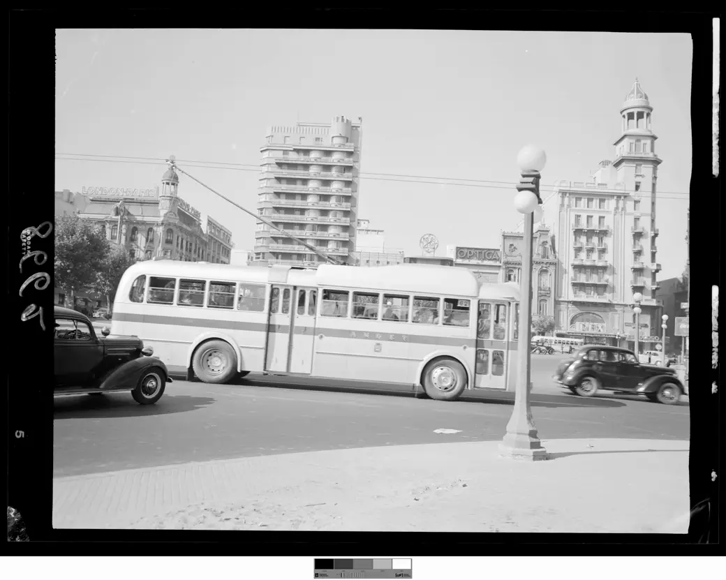 Un trolebús con las letras AMDET y el cartel 62 circula por la calle Colonia entre autos de la época, bajo los cables aéreos; detrás, edificios altos, y un farol en primer plano.
