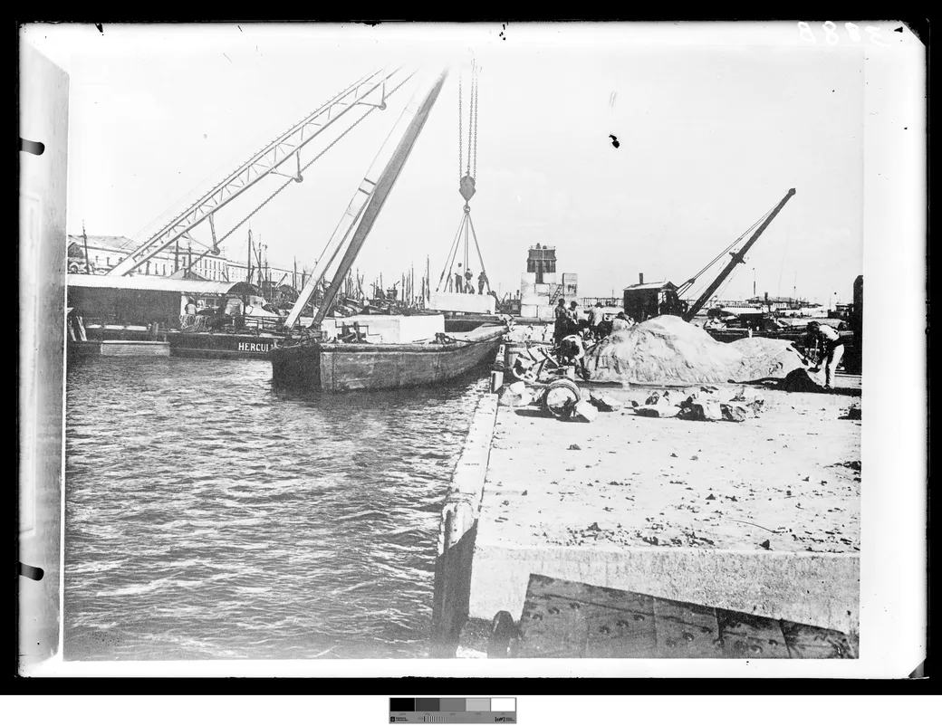 Foto histórica, 1901-1909: la construcción del puerto, con una grúa pasando piedra labrada de la barcaza al muelle y una segunda barcaza amarrada al costado.