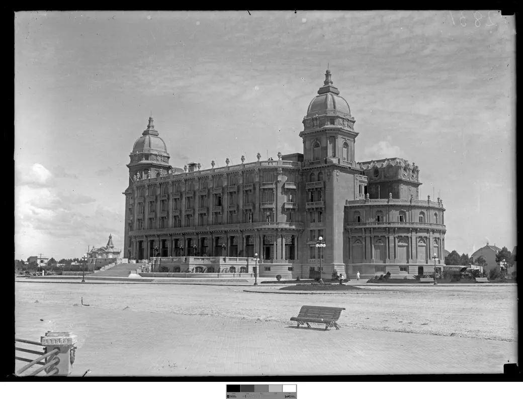 Foto histórica, 1921: el Hotel Carrasco recién inaugurado, de pie sobre una vasta extensión de arena vacía, con un banco de madera en primer plano.