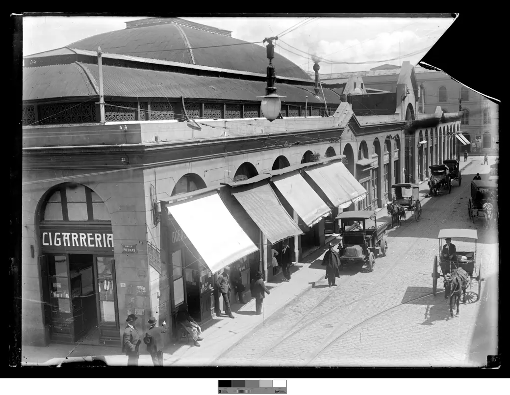 Foto histórica, hacia 1915: la esquina de Piedras y Pérez Castellano, con la arcada de hierro y vidrio del Mercado del Puerto, toldos, una cigarrería y un carro a caballo.