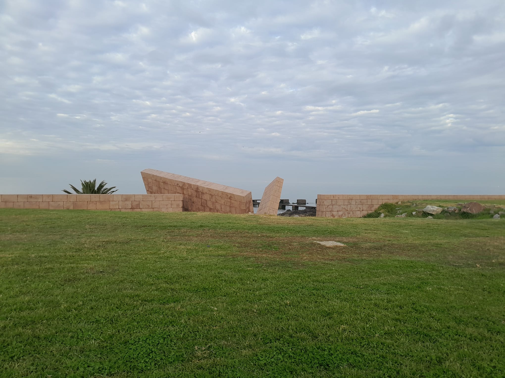 El muro del Memorial del Holocausto visto de frente, sobre el pasto que da al río.