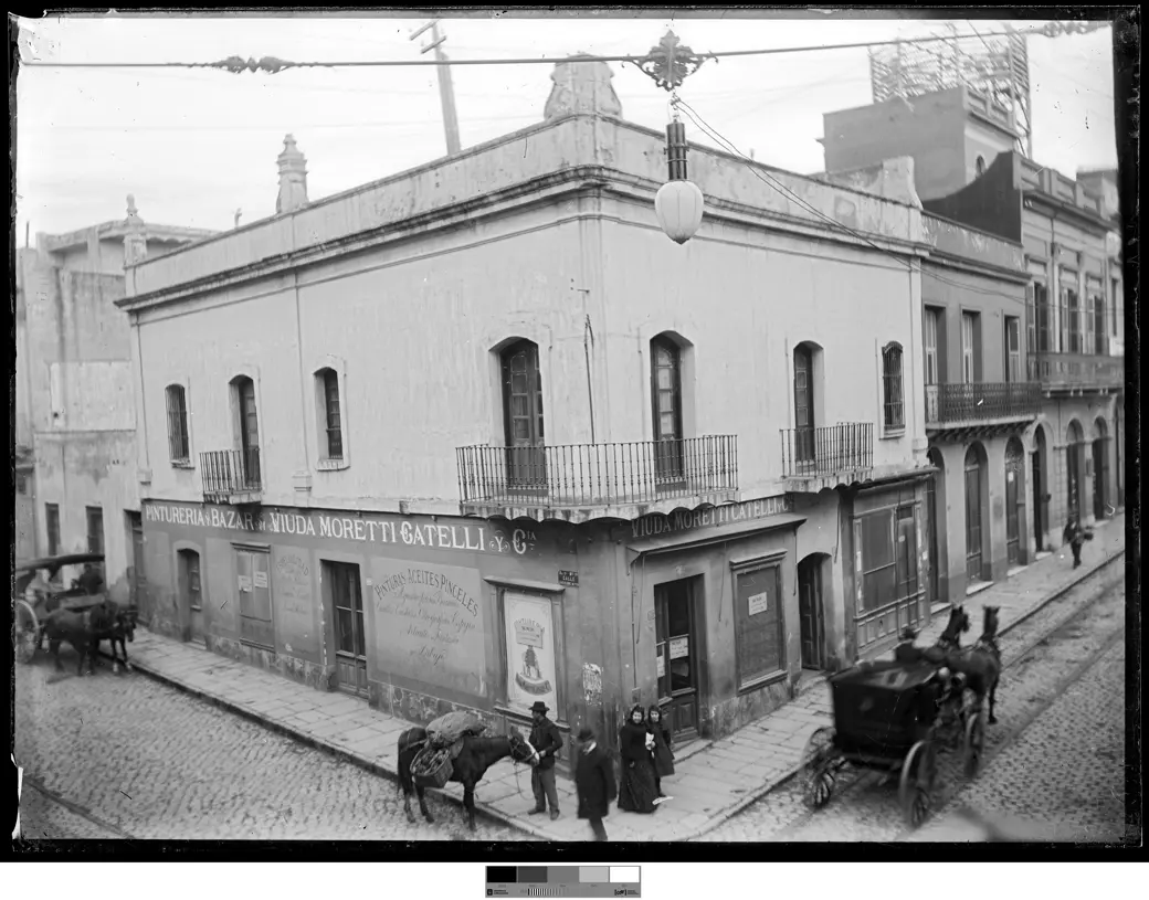 Foto histórica, hacia 1900: la esquina de Rincón y Bartolomé Mitre, con carros a ambos lados y peatones caminando directamente sobre el adoquinado.