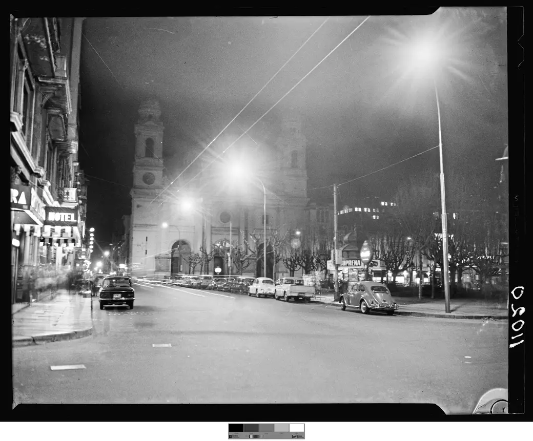 Foto histórica, agosto de 1966: autos contra el cordón frente a la Plaza Constitución, con la torre iluminada de la Iglesia Matriz al fondo.